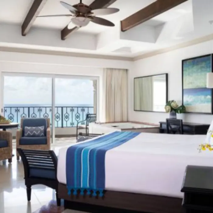 Bright oceanfront suite with king bed, cozy seating area, and glass doors to private balcony.