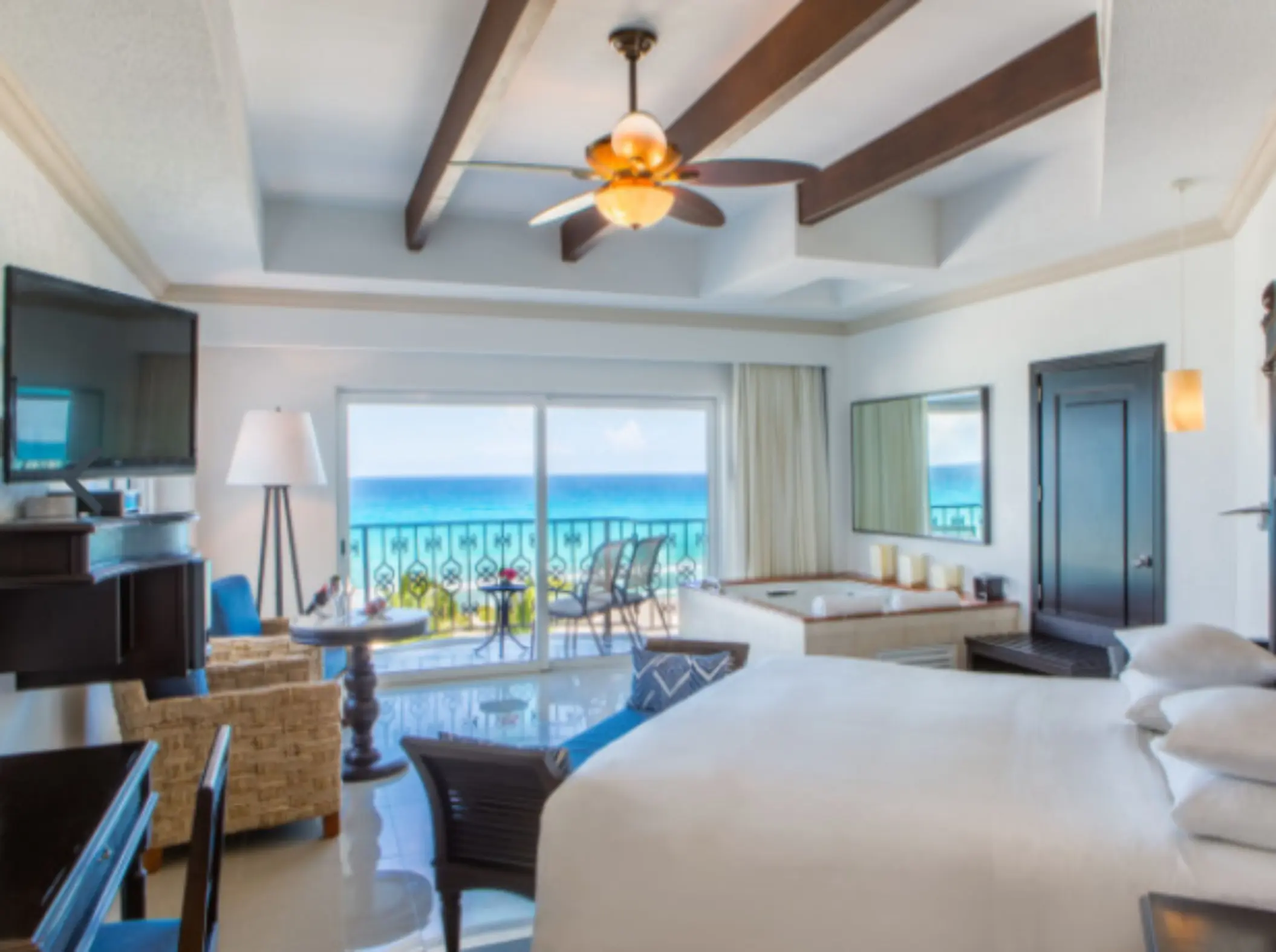 Spacious suite with ocean view, ceiling fan, hot tub, and balcony access through sliding doors.