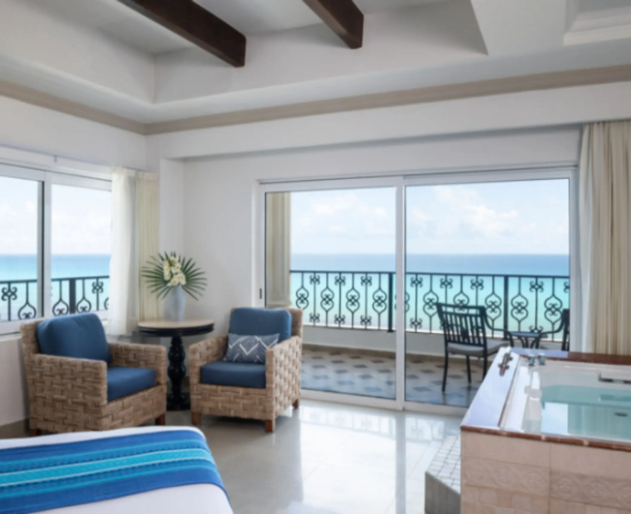 Corner suite with twin blue chairs, ocean view from two sides, and in-room hot tub.
