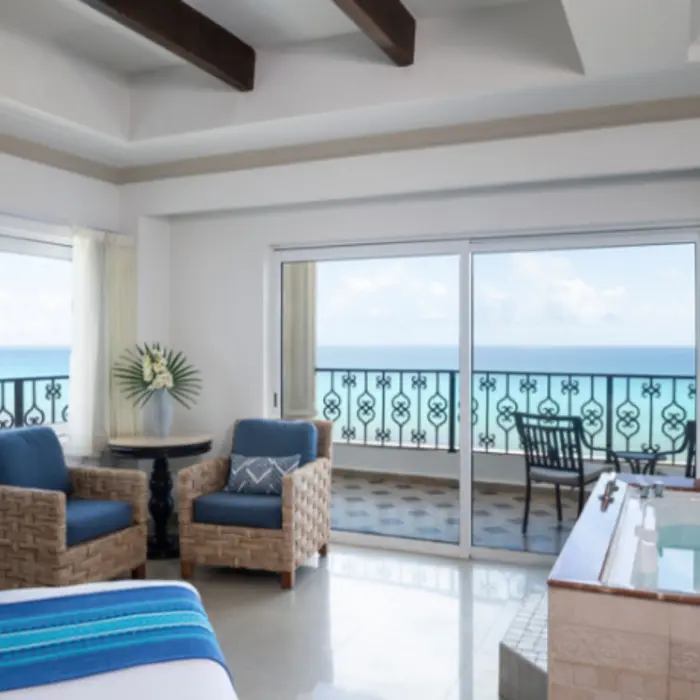 Corner suite with twin blue chairs, ocean view from two sides, and in-room hot tub.
