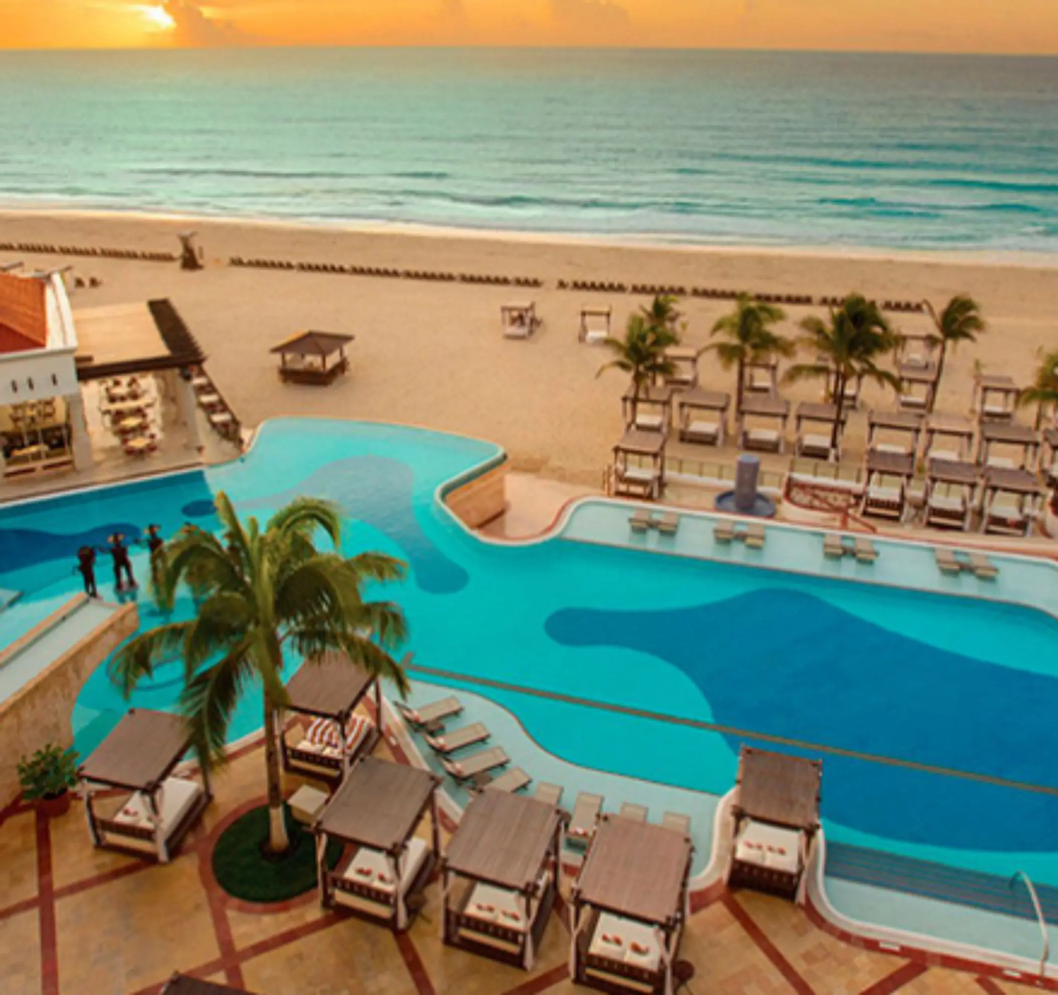 Infinity pool overlooking the beach with daybeds and ocean views during a golden Caribbean sunset.