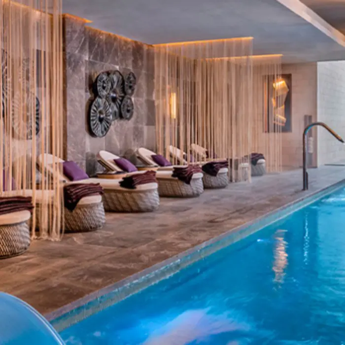 Relaxation area in the spa with loungers and soft lighting next to a serene indoor pool.