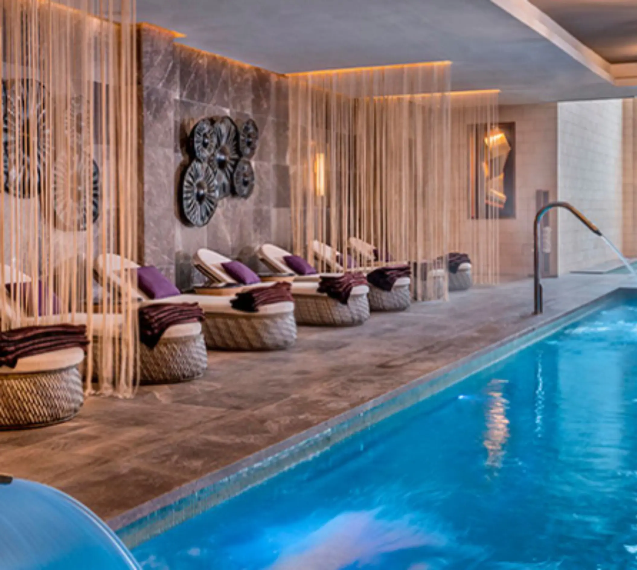 Relaxation area in the spa with loungers and soft lighting next to a serene indoor pool.