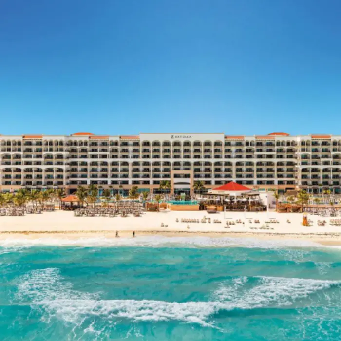 Oceanfront resort view showcasing balconies, beach loungers, and turquoise waves under a blue sky.