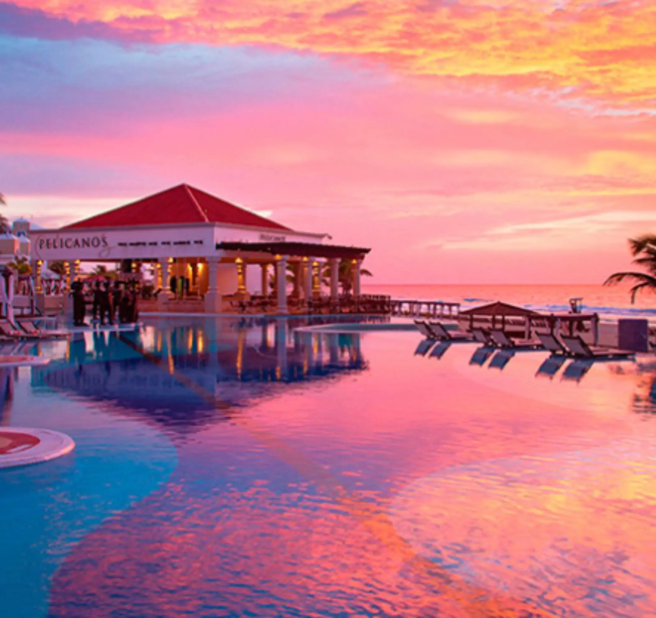 Pelicanos restaurant by the pool at sunset, with vibrant skies reflecting over calm turquoise waters.