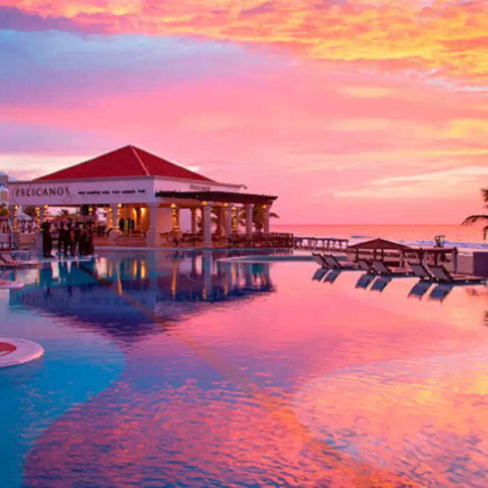 Pelicanos restaurant by the pool at sunset, with vibrant skies reflecting over calm turquoise waters.