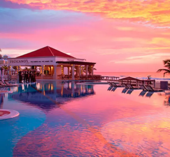 Pelicanos restaurant by the pool at sunset, with vibrant skies reflecting over calm turquoise waters.