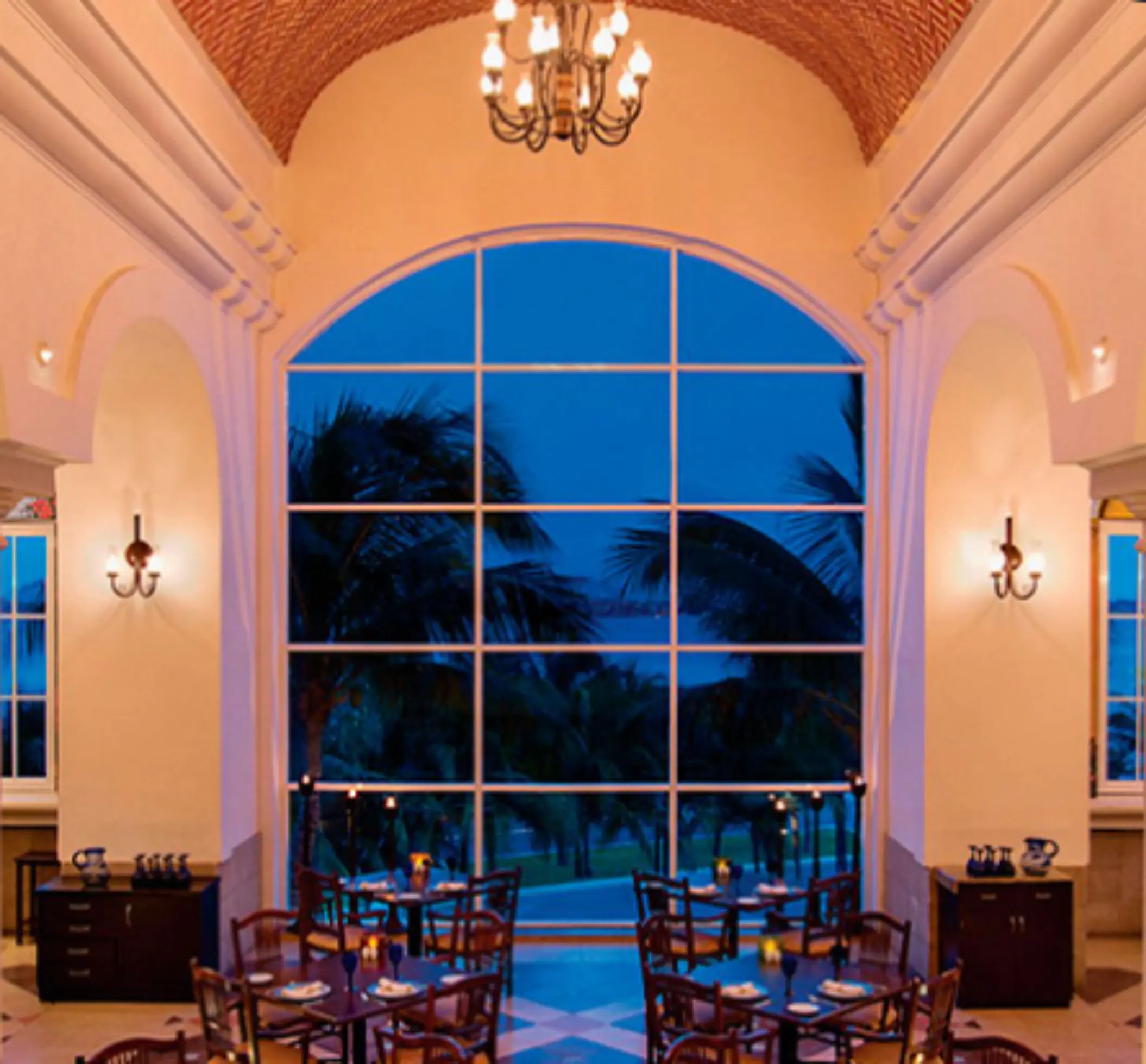 Dining area with ocean views, modern decor, and wooden furniture set against a backdrop of palm trees and loungers.