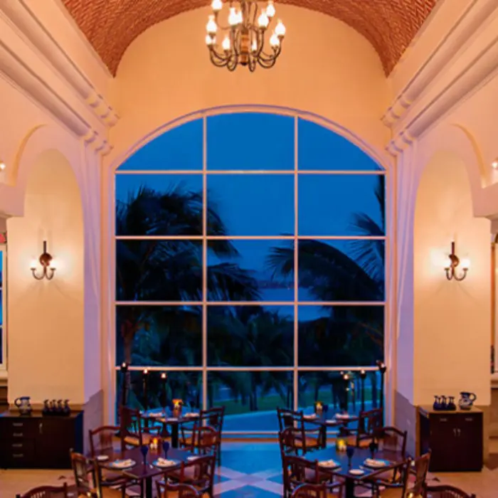 Dining area with ocean views, modern decor, and wooden furniture set against a backdrop of palm trees and loungers.