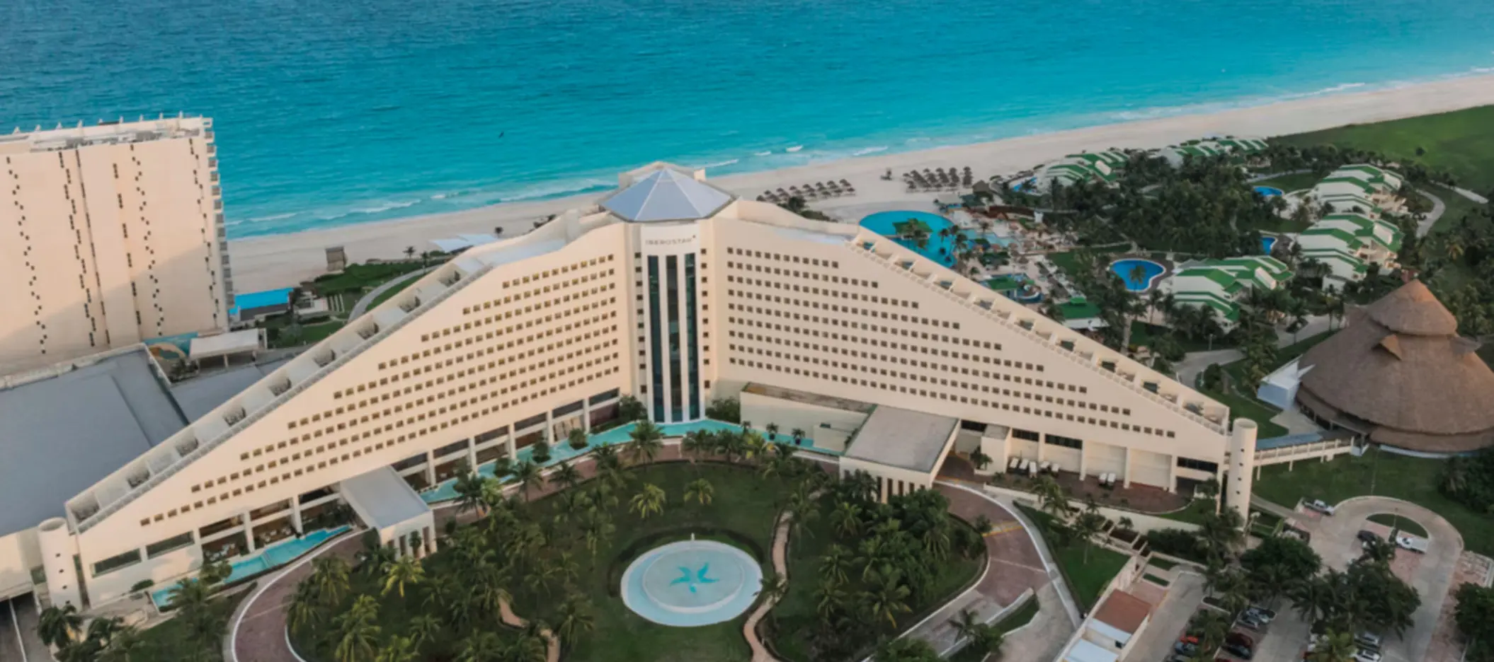 Panoramic aerial view of a beachfront resort with triangular hotel facade, pools, and turquoise Caribbean waters.