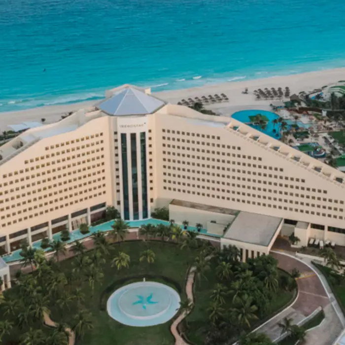 Panoramic aerial view of a beachfront resort with triangular hotel facade, pools, and turquoise Caribbean waters.
