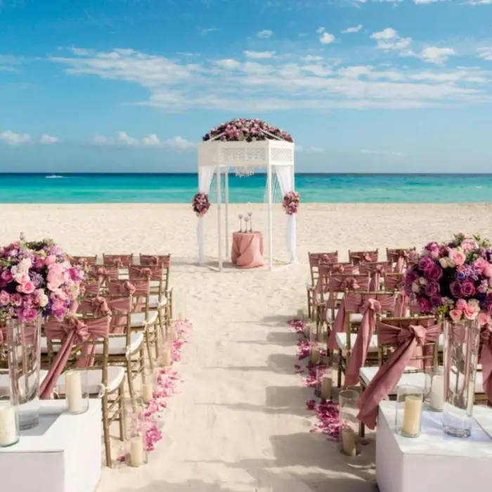 A beach wedding setup with a white arbor, rows of chairs, and pink flowers overlooking the sea.