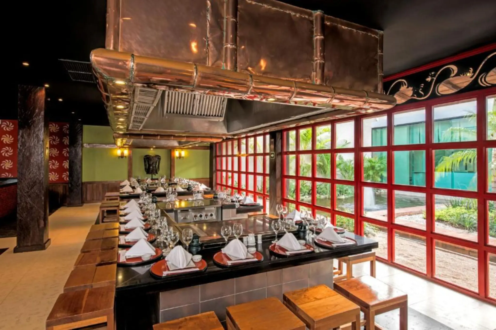 A modern restaurant with a long table, chairs, and a large hood over a cooking station.