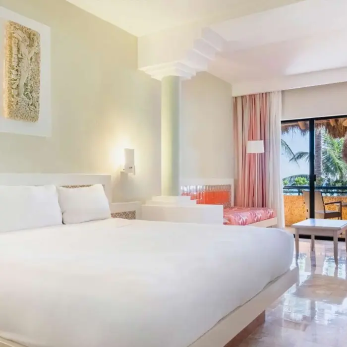 A hotel suite with a large bed and a balcony that overlooks the tropical gardens.