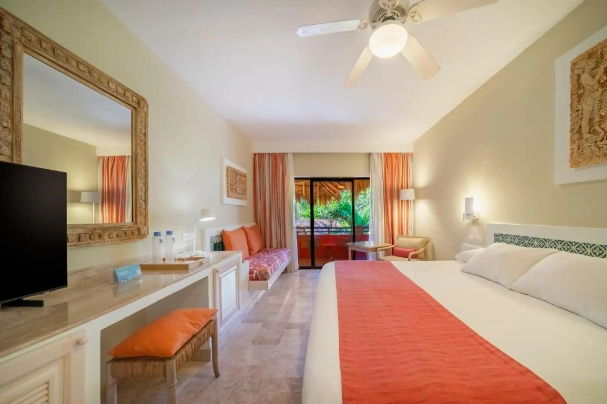 A guest room with a bed, a desk, a television, and a balcony with a garden view.