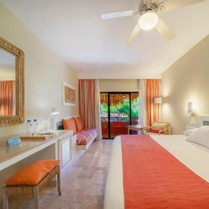 A guest room with a bed, a desk, a television, and a balcony with a garden view.