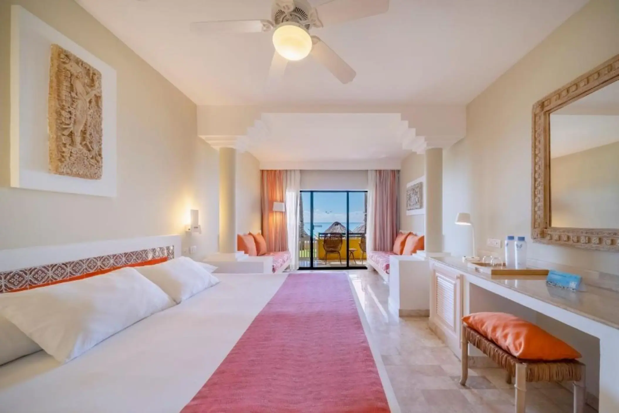 A bright suite with a bed, a desk, and a balcony with an ocean view.