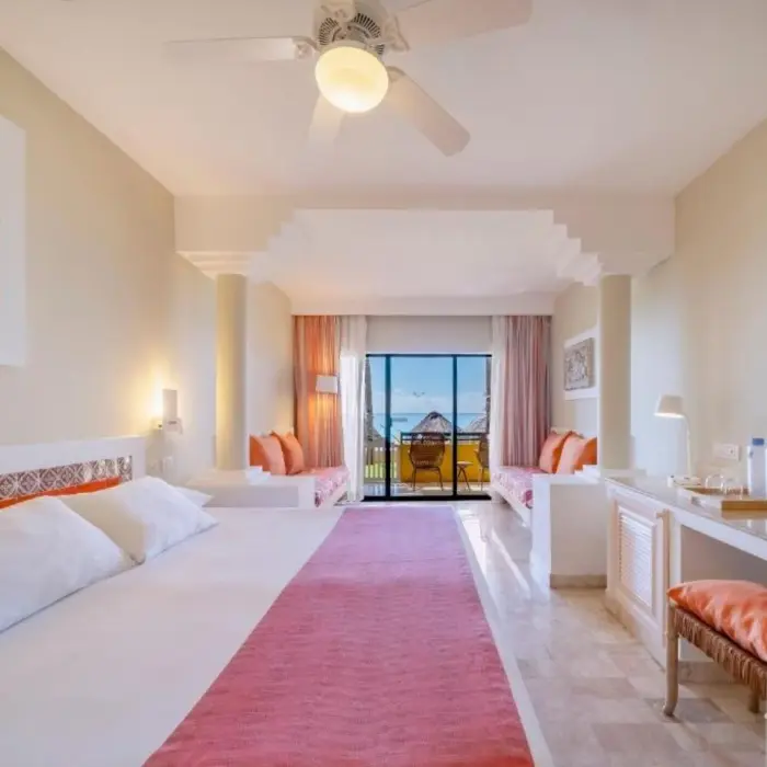 A bright suite with a bed, a desk, and a balcony with an ocean view.