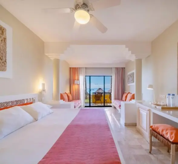 A bright suite with a bed, a desk, and a balcony with an ocean view.