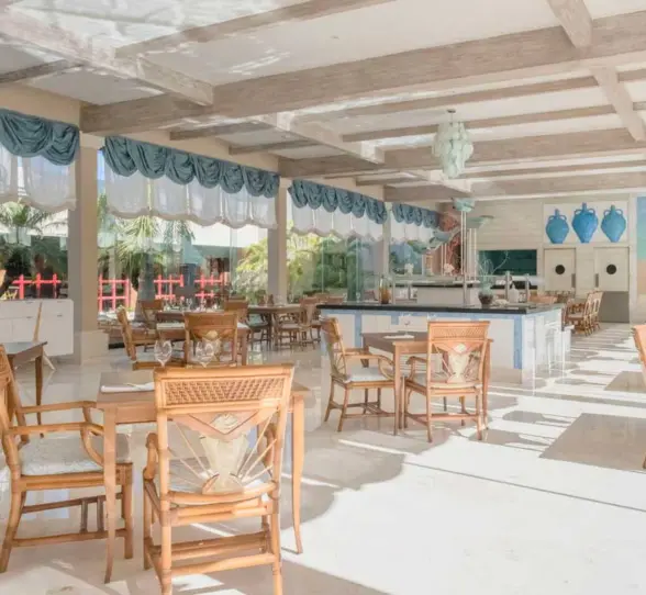 A well-lit restaurant with wooden tables and chairs, decorative blue accents, and large windows.