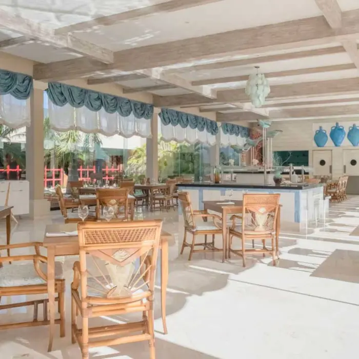 A well-lit restaurant with wooden tables and chairs, decorative blue accents, and large windows.