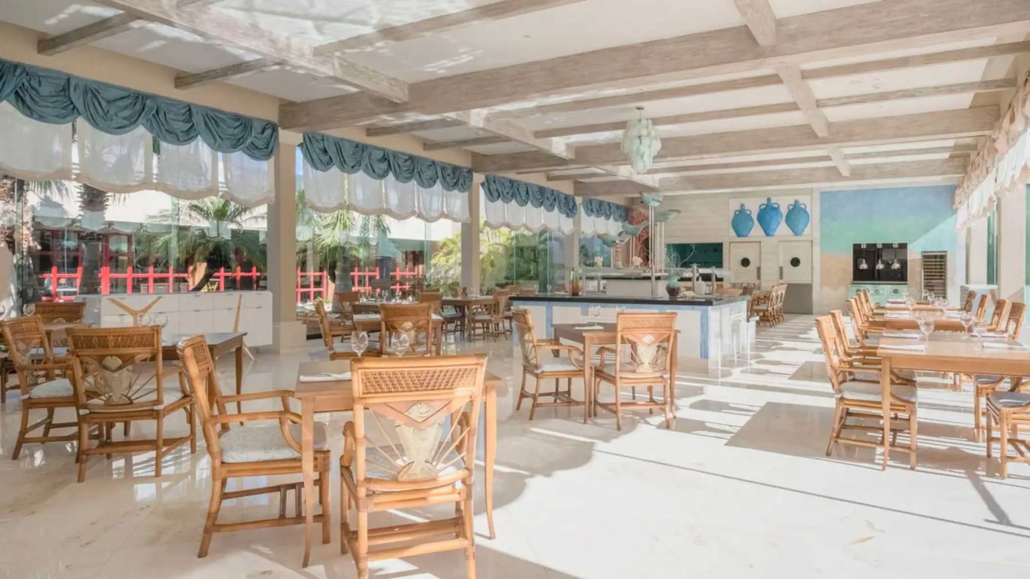 A well-lit restaurant with wooden tables and chairs, decorative blue accents, and large windows.