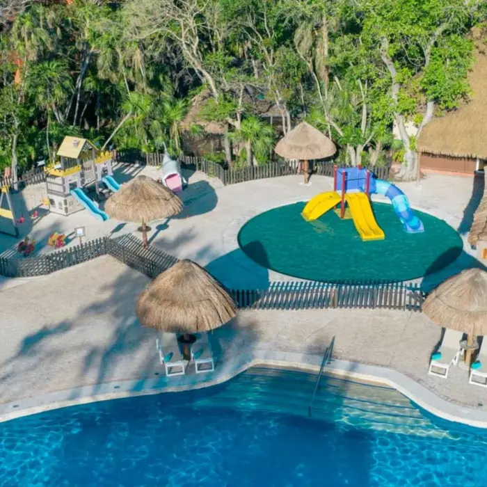 An aerial view of a resort pool next to a colorful children's playground with slides and swings.