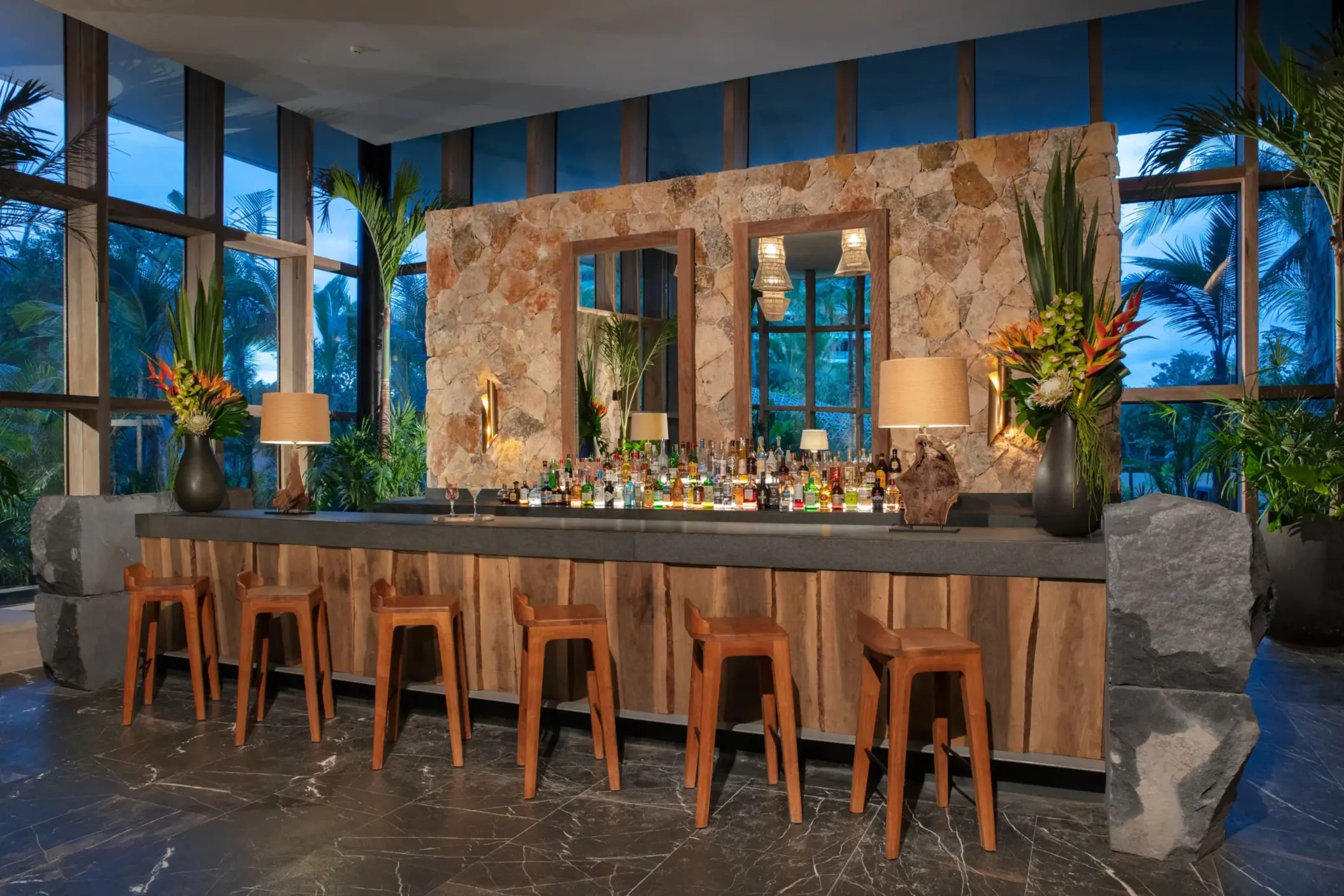 Cozy lobby bar with wooden stools, stone walls, and tropical décor.
