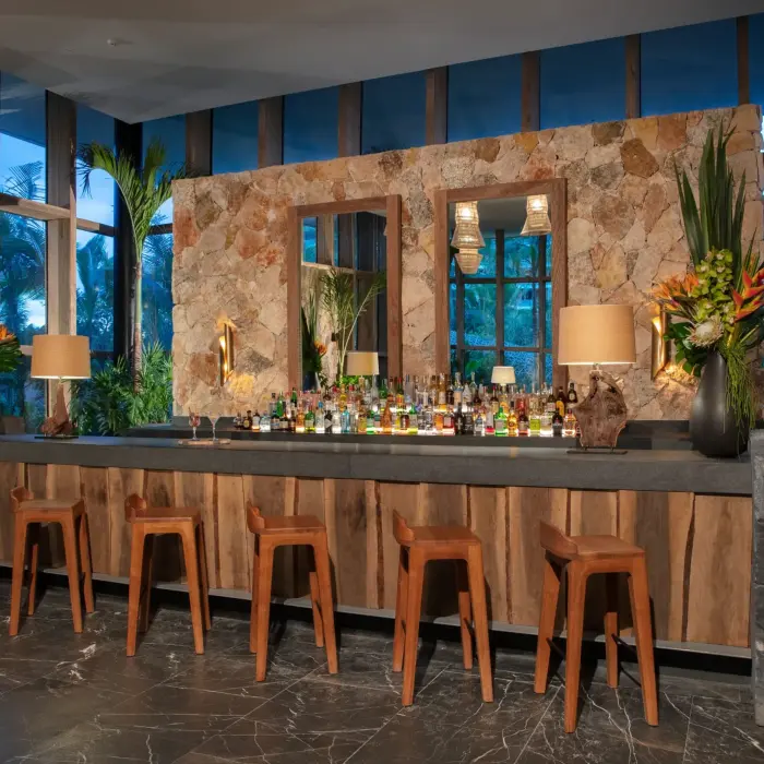 Cozy lobby bar with wooden stools, stone walls, and tropical décor.
