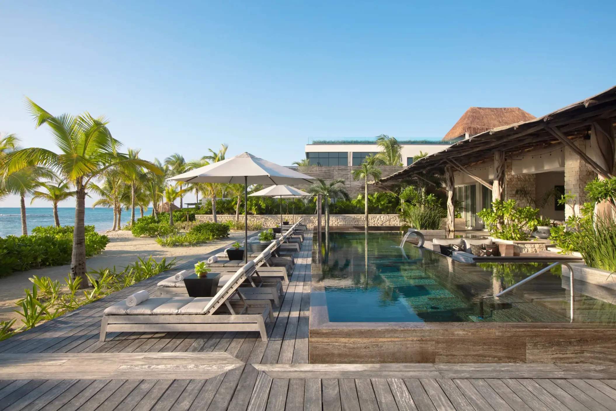 Private beachfront pool lined with loungers and umbrellas, steps from the ocean.