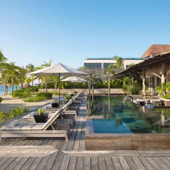 Private beachfront pool lined with loungers and umbrellas, steps from the ocean.