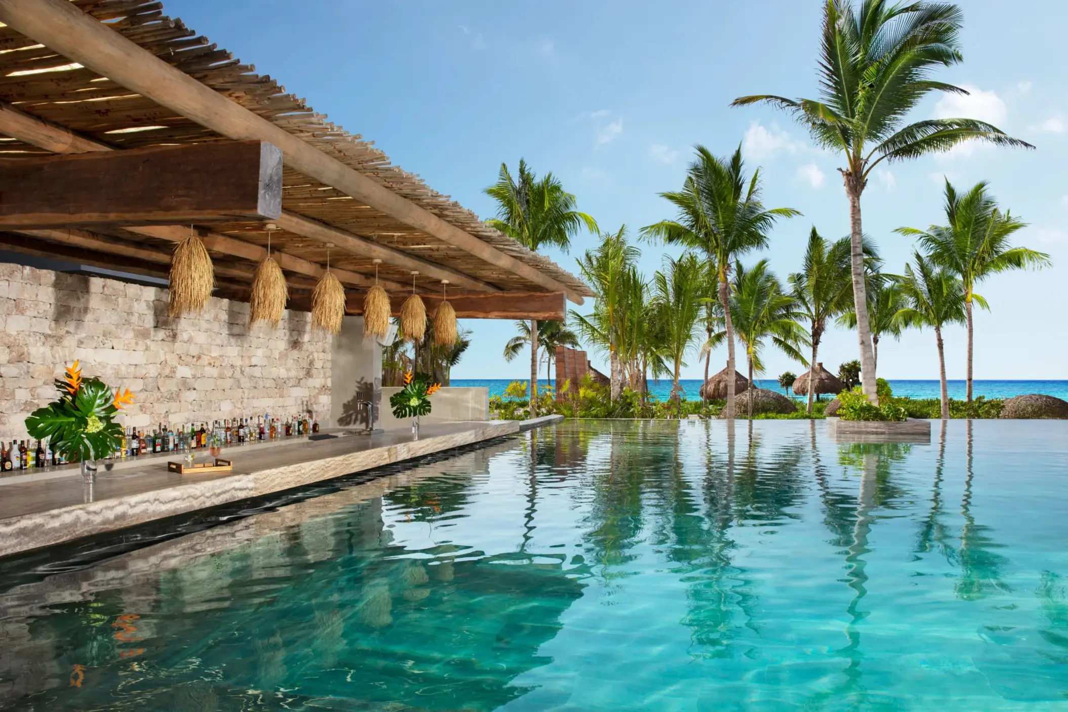 Swim-up pool bar with tropical decor, rustic stone walls, and ocean views.