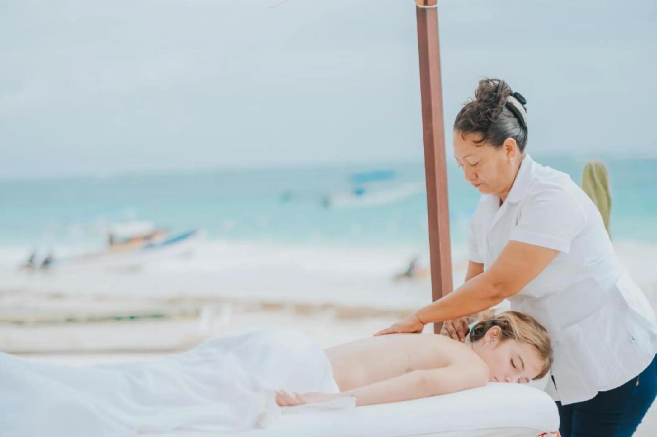 A woman receiving a relaxing beachside massage at Kai Tulum Hotel spa, with the ocean in the background.
