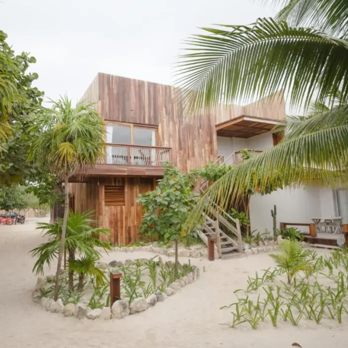 Exteriors of the suites at Kai Tulum Hotel, with wooden facades, balconies, and sandy pathways amidst lush plants.
