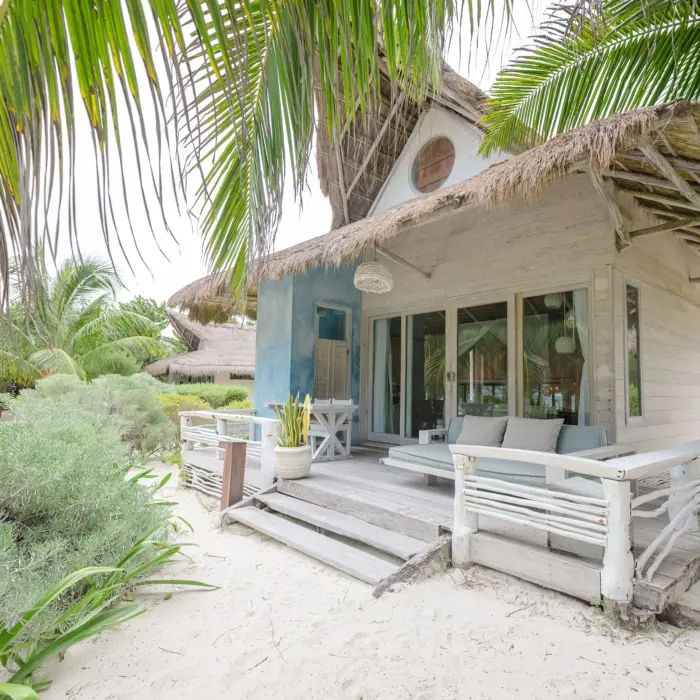 The exterior of an oceanfront suite at Kai Tulum Hotel, featuring a rustic design with a thatched roof and patio.
