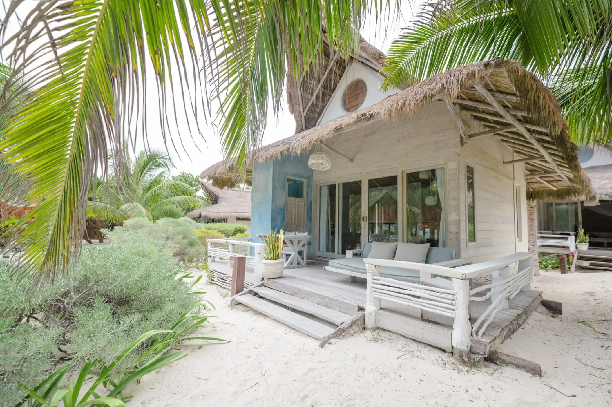 The exterior of an oceanfront suite at Kai Tulum Hotel, featuring a rustic design with a thatched roof and patio.