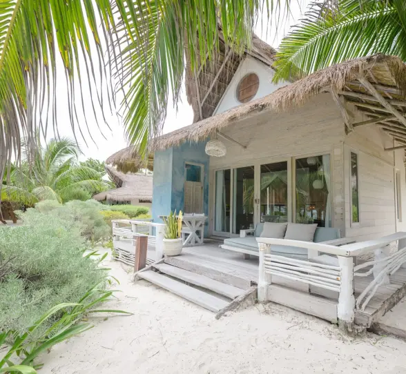 The exterior of an oceanfront suite at Kai Tulum Hotel, featuring a rustic design with a thatched roof and patio.