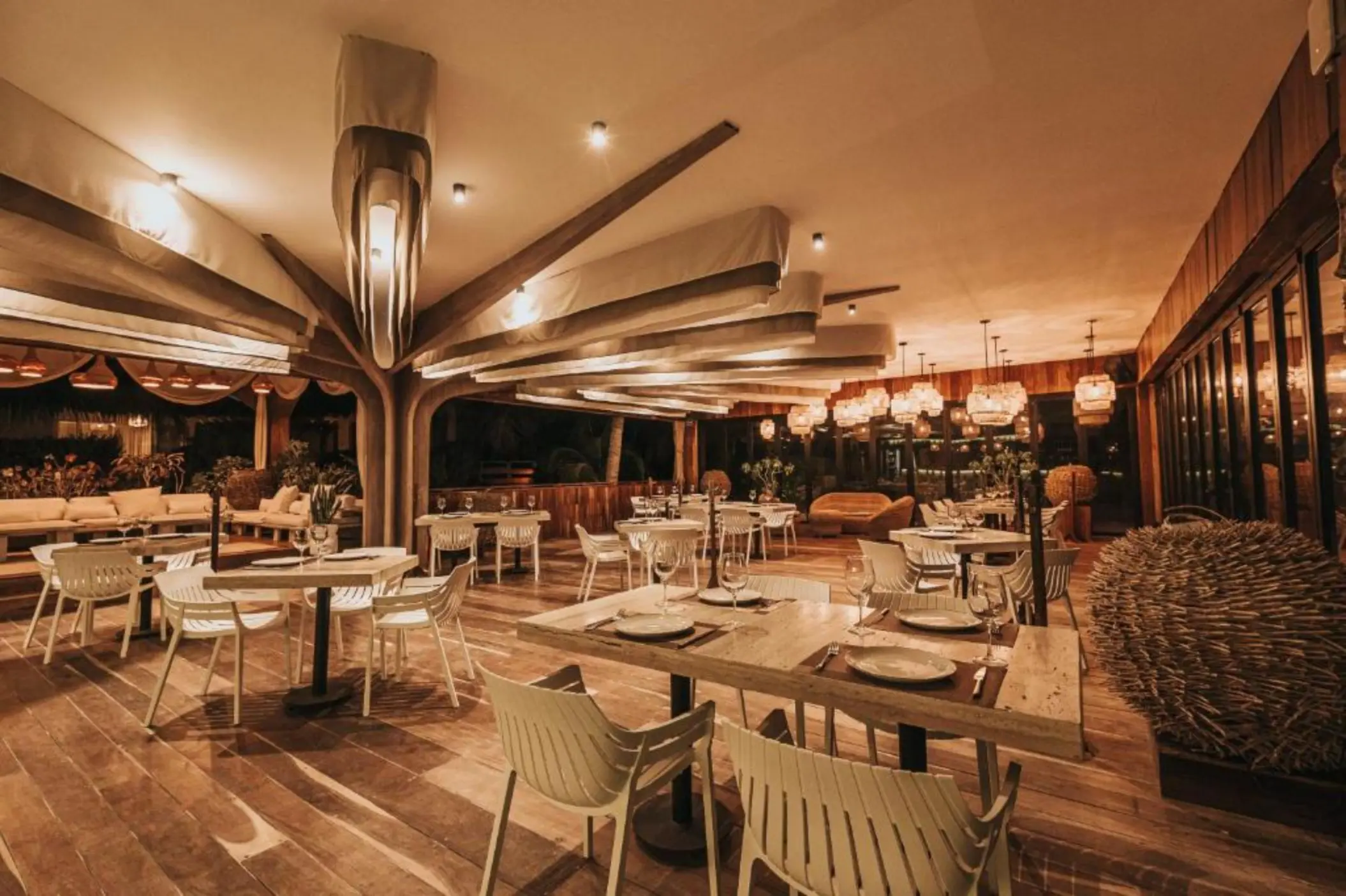 The modern-rustic Kai Restaurant at Kai Tulum Hotel, with unique lighting, wooden floors, and white seating.