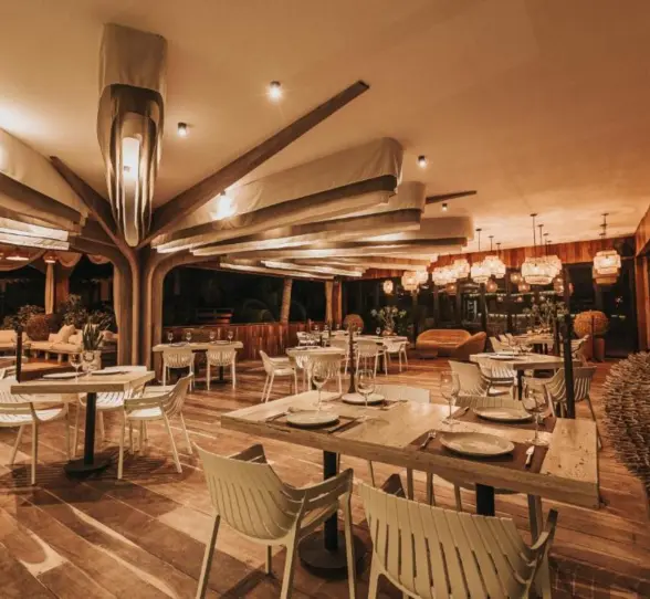 The modern-rustic Kai Restaurant at Kai Tulum Hotel, with unique lighting, wooden floors, and white seating.
