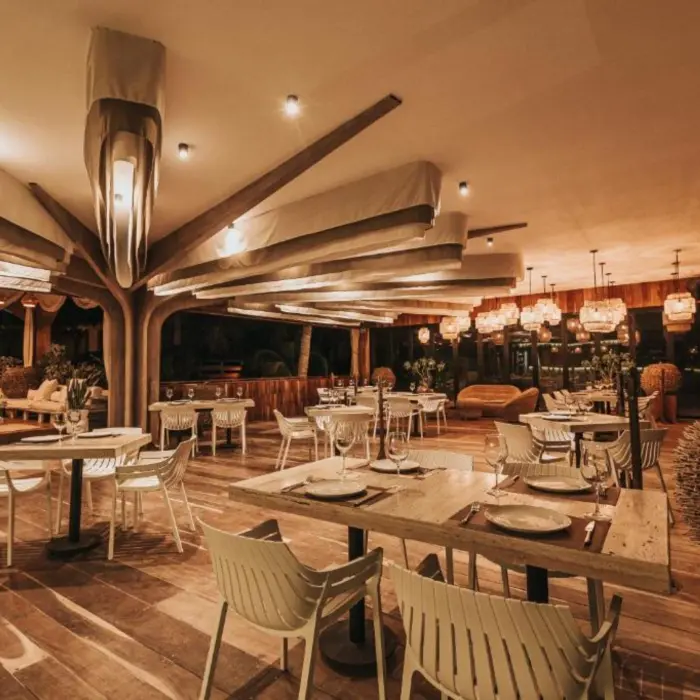 The modern-rustic Kai Restaurant at Kai Tulum Hotel, with unique lighting, wooden floors, and white seating.