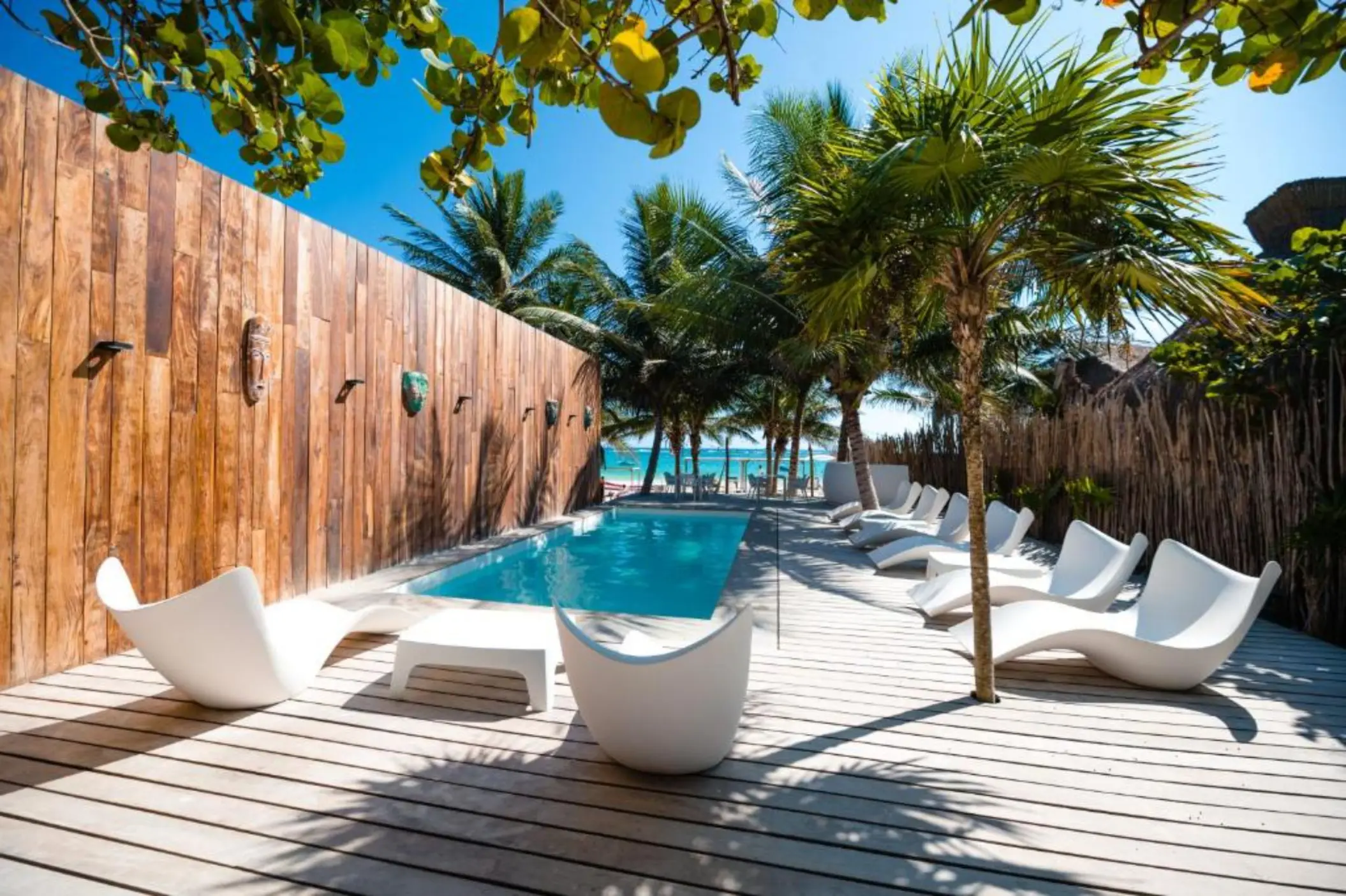 A serene swimming pool at Kai Tulum Hotel, surrounded by white lounge chairs, palm trees, and a wooden deck.