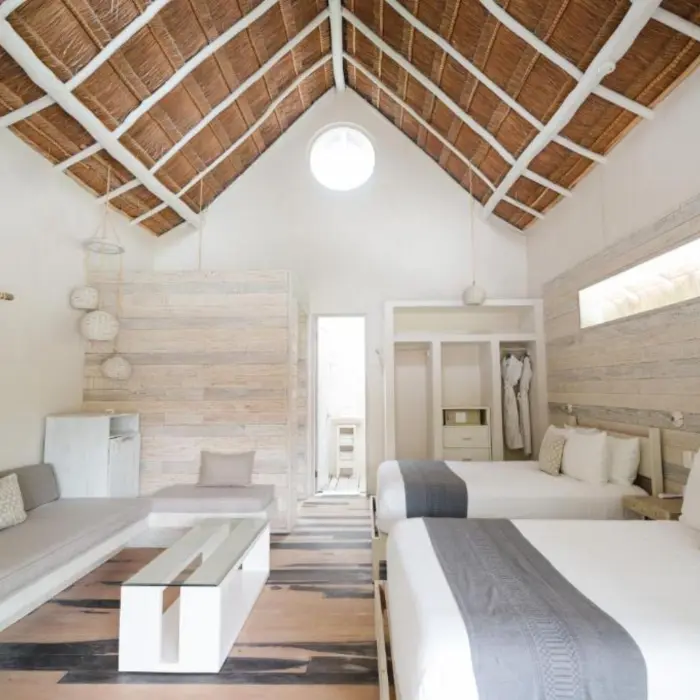 A spacious suite at Kai Tulum Hotel with two beds, a thatched roof, and natural wood accents.