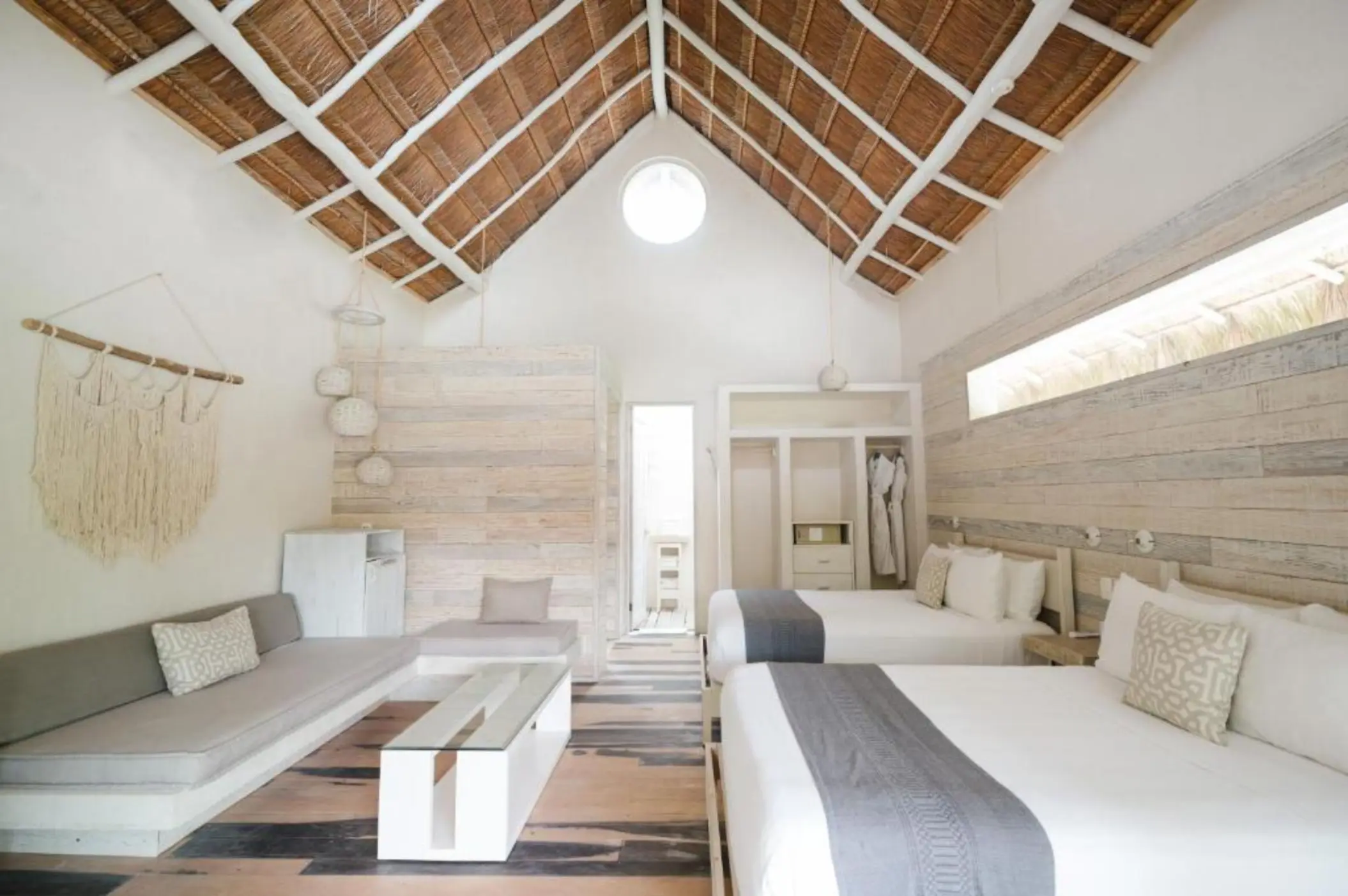 A spacious suite at Kai Tulum Hotel with two beds, a thatched roof, and natural wood accents.