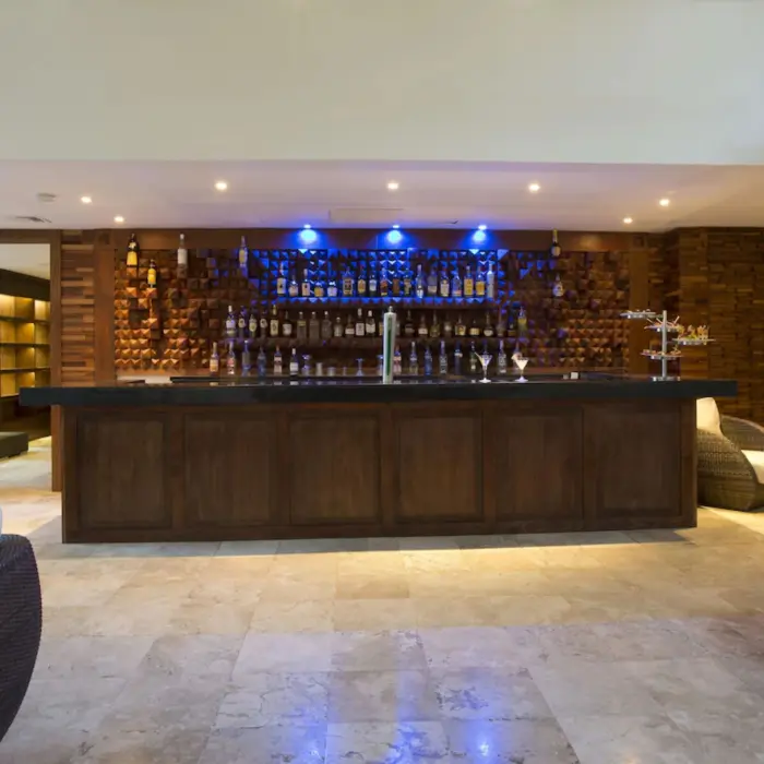 A stylish hotel bar with a long wooden counter, a well-stocked liquor display, and comfortable seating.