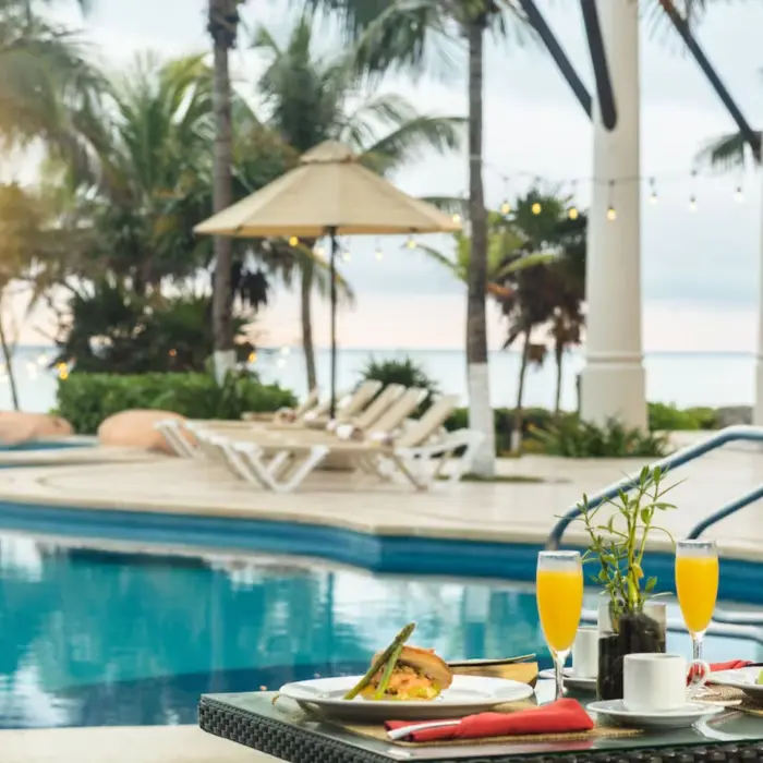 A delicious breakfast spread with mimosas on a table next to a sparkling pool, with ocean views.