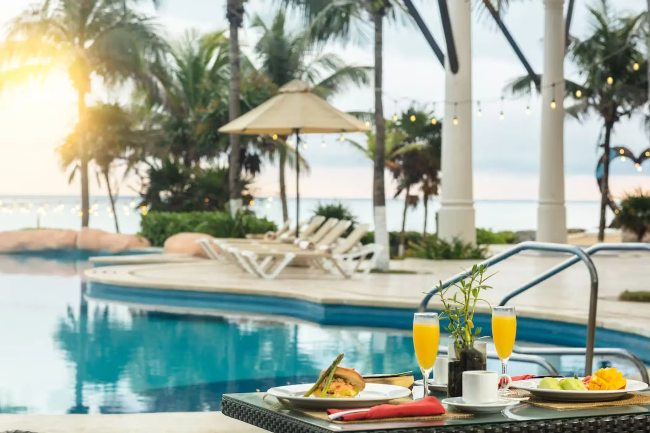 A delicious breakfast spread with mimosas on a table next to a sparkling pool, with ocean views.