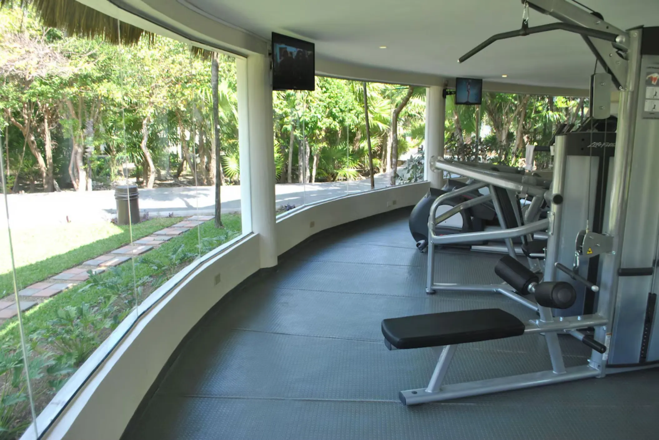 A modern gym with various exercise machines, featuring large windows overlooking lush greenery.