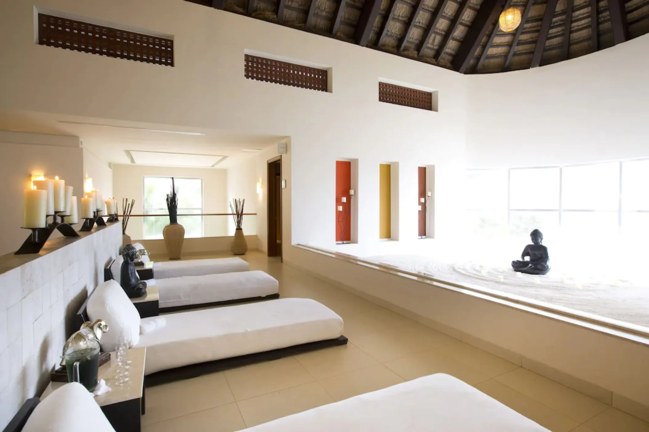 A serene spa relaxation area with recliners, candles, and a large Buddha statue in a sand garden.