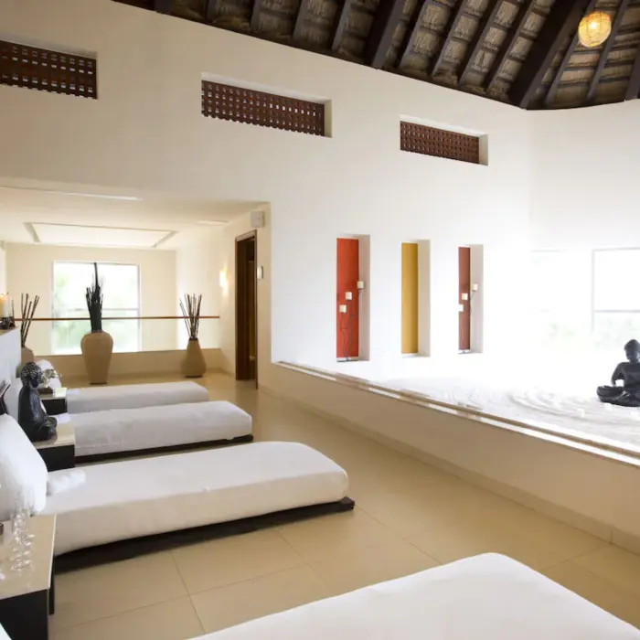 A serene spa relaxation area with recliners, candles, and a large Buddha statue in a sand garden.