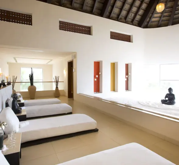 A serene spa relaxation area with recliners, candles, and a large Buddha statue in a sand garden.